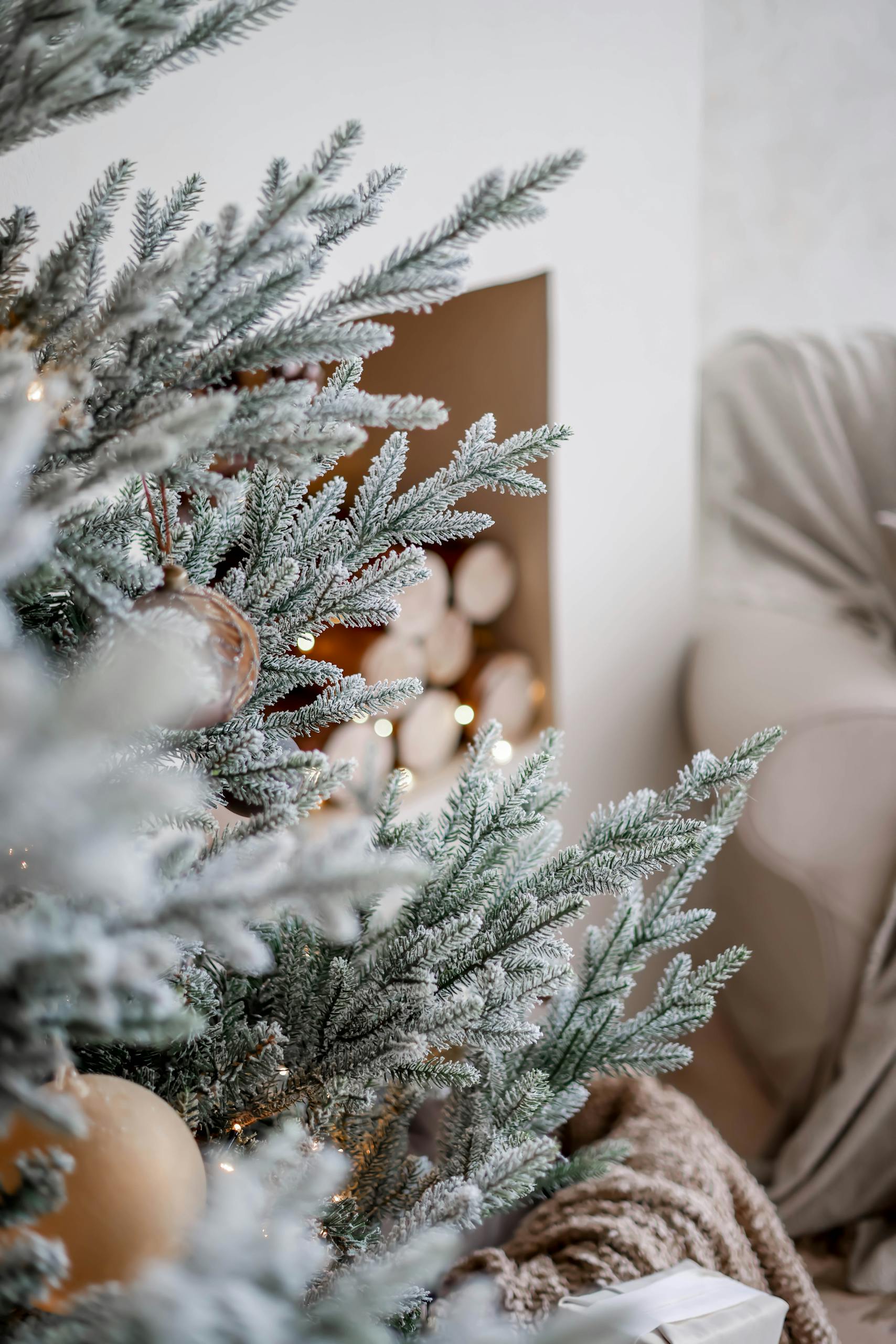 Close-up of an elegantly decorated Christmas tree with frosty needles in a cozy living room setting.