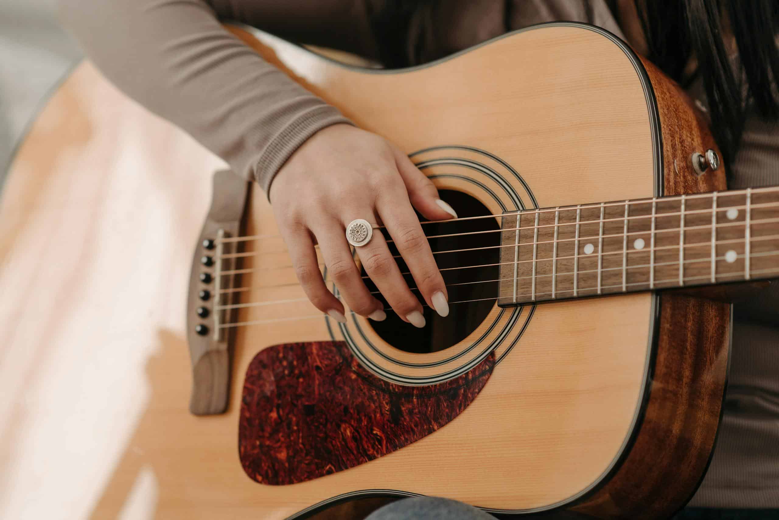 A close-up of a woman's hand strumming an acoustic guitar, showcasing musical passion.